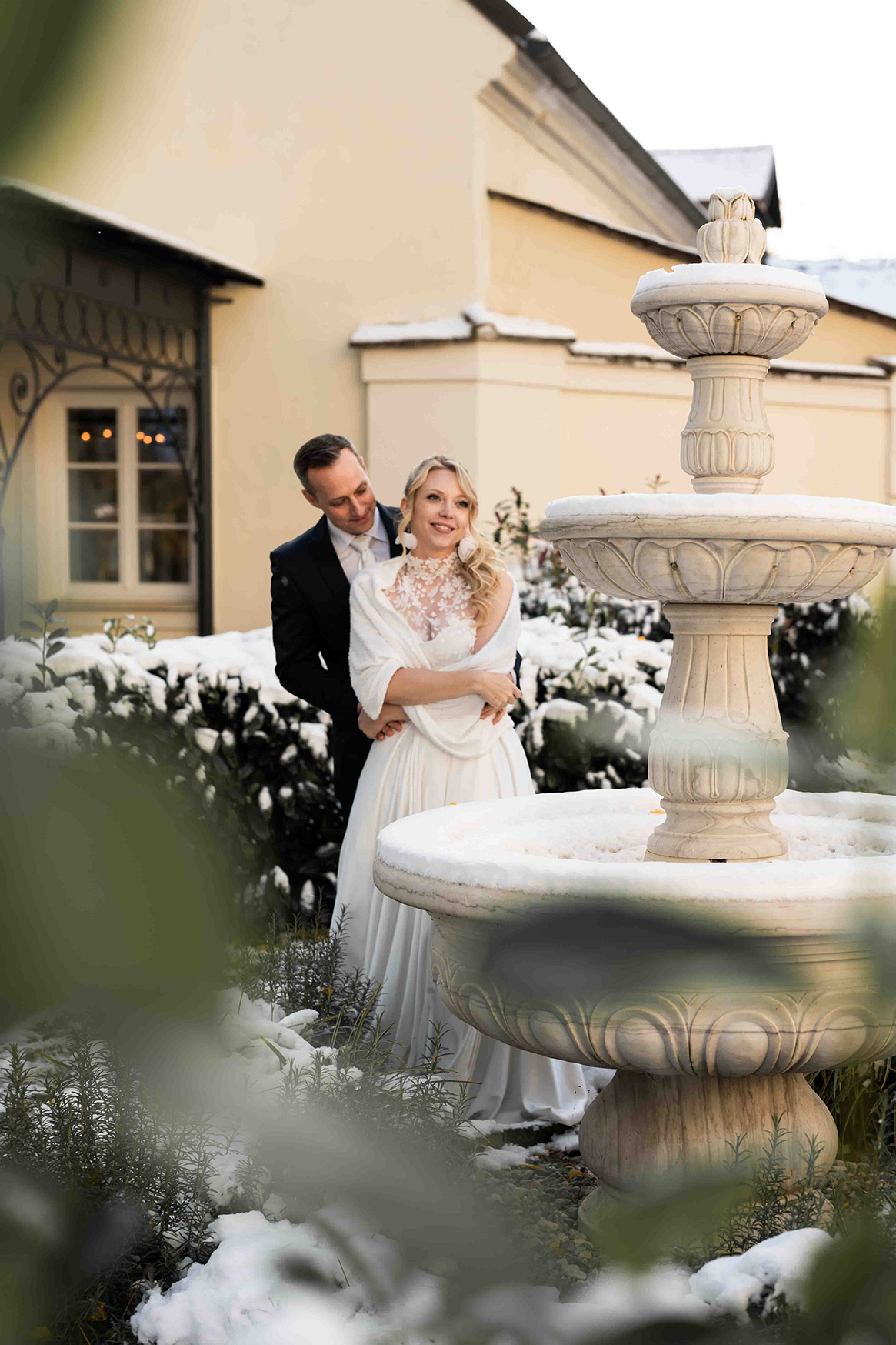 Brautpaar, Mann im schwarzen Hochzeitsanzug, Frau in weißem Hochzeitskleid bei winterlichen Verhältnissen beim Brunnen im Schloss Gurhof