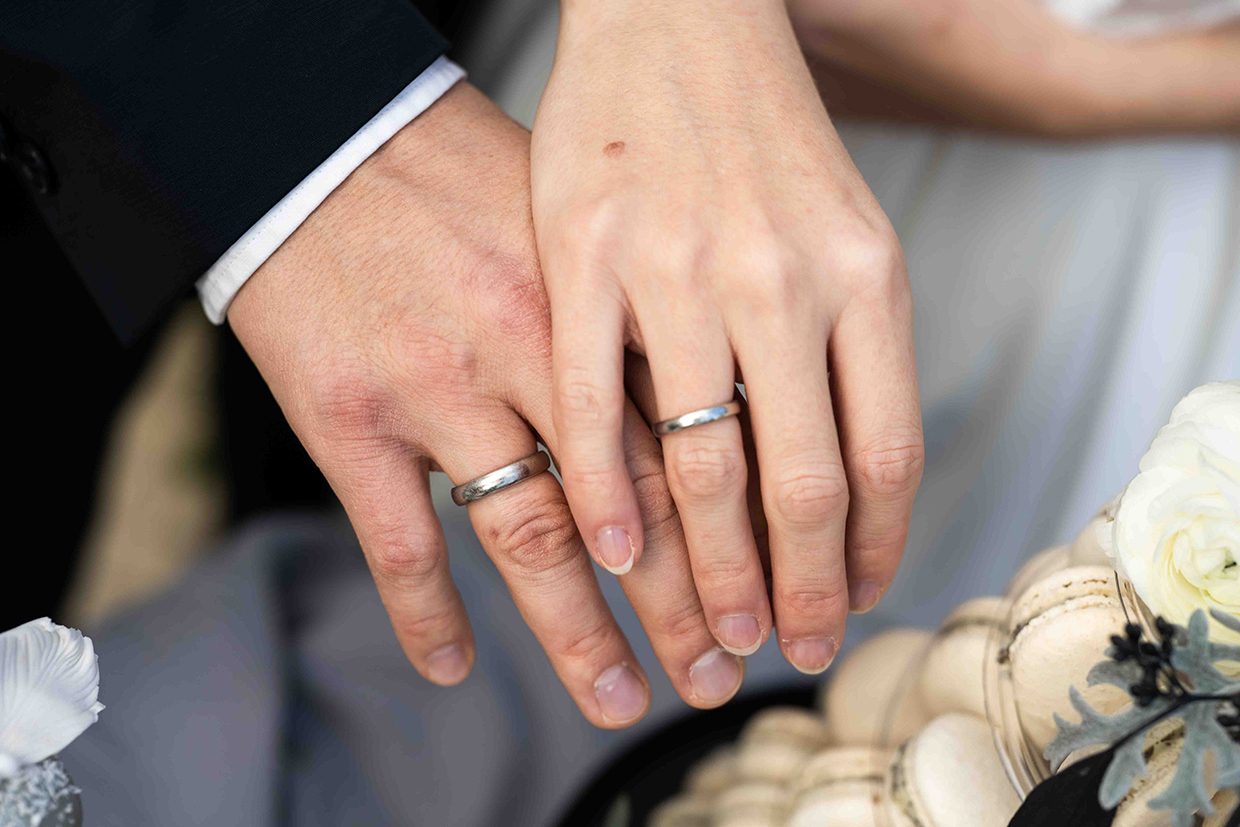 Brautpaar, Mann im schwarzen Hochzeitsanzug, Frau in weißem Hochzeitskleid kuschelnde Hände mit den wundervollen Eheringen im Schloss Gurhof