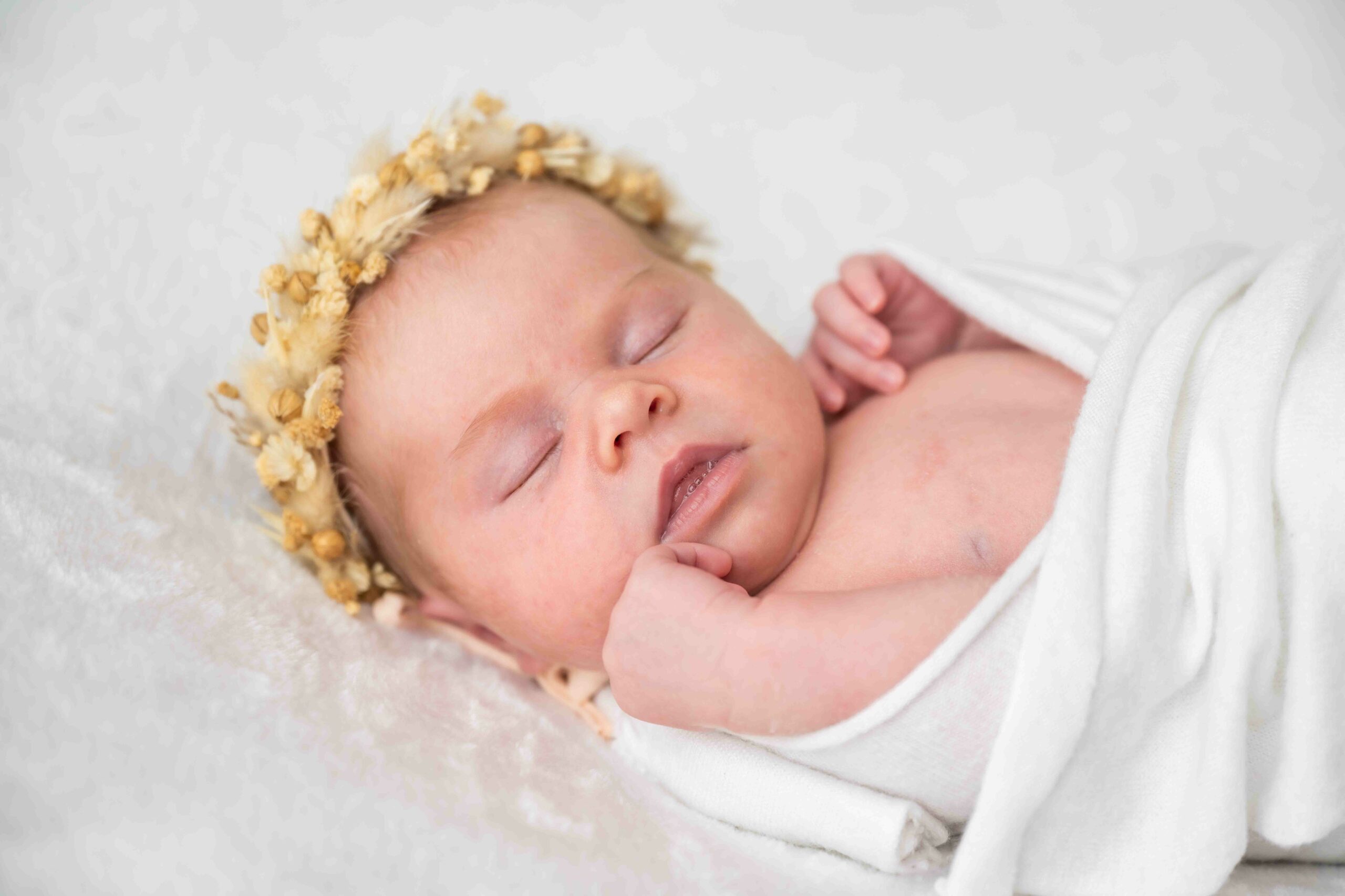 Babymädchen in weißes Tuch gehüllt mit Strohkranz am Kopf, seitlich fotografiert