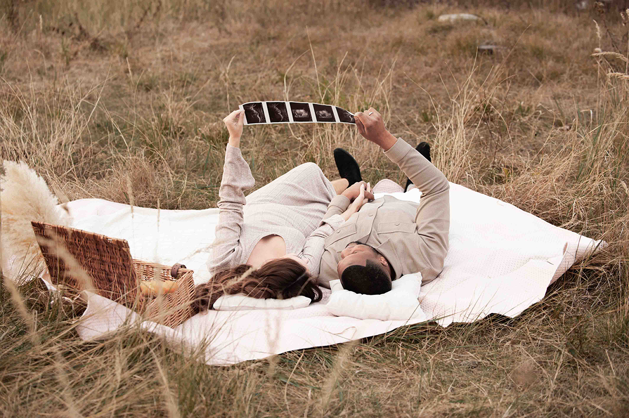 Liebendes Pärchen (Mann und seine wundervolle Frau) liegen auf einer Picknickdecke und betrachten Ihre Schwangerschaft ultraschallbilder und sind voller Vorfreude auf Ihren Nachwuchs!