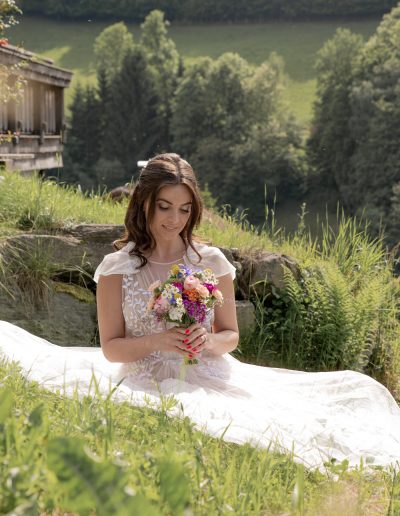 Braut mit Blumenstrauß sitzt auf einer Wiese