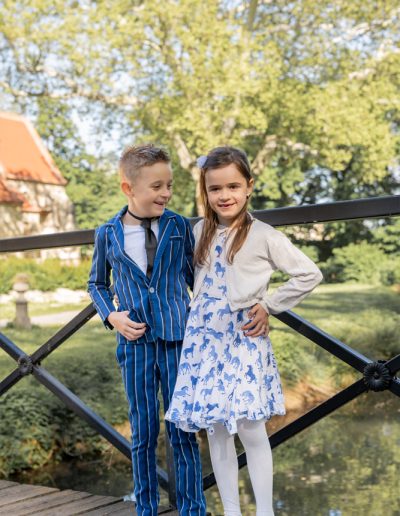 Mädchen in Kleid und Bub in blauem Anzug auf einer Parkbrücke