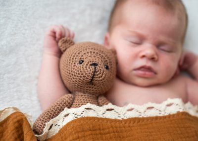 Neugeborenes Baby mit gehäkeltem Teddybär