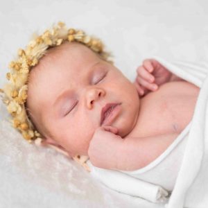 Babymädchen in weißes Tuch gehüllt mit Strohkranz am Kopf, seitlich fotografiert
