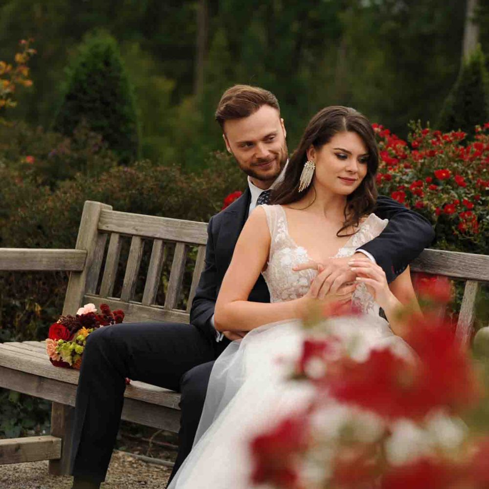 Brautpaar, Mann im schwarzen Hochzeitsanzug, Frau in weißem Hochzeitskleid im Herbst auf einer Parkbank im Freien im Schloss Eckertsau