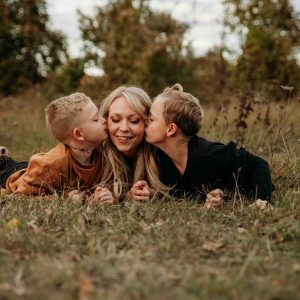 Mama wird von Ihren beiden Kindern auf die Wangen geküsst, sie befinden sich in herbstlicher Landschaft