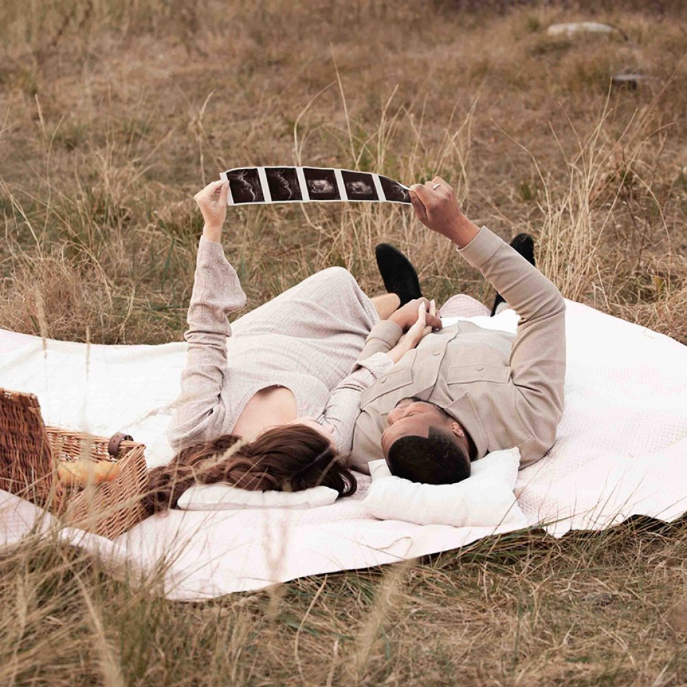 Liebendes Pärchen (Mann und seine wundervolle Frau) liegen auf einer Picknickdecke und betrachten Ihre Schwangerschaft ultraschallbilder und sind voller Vorfreude auf Ihren Nachwuchs!